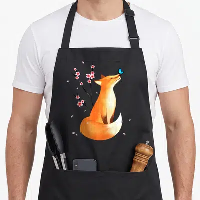 Cherry fox print apron - Orange fox sitting under pink cherry blossoms with blue butterfly on nose — shown on a black cotton canvas apron against a white background