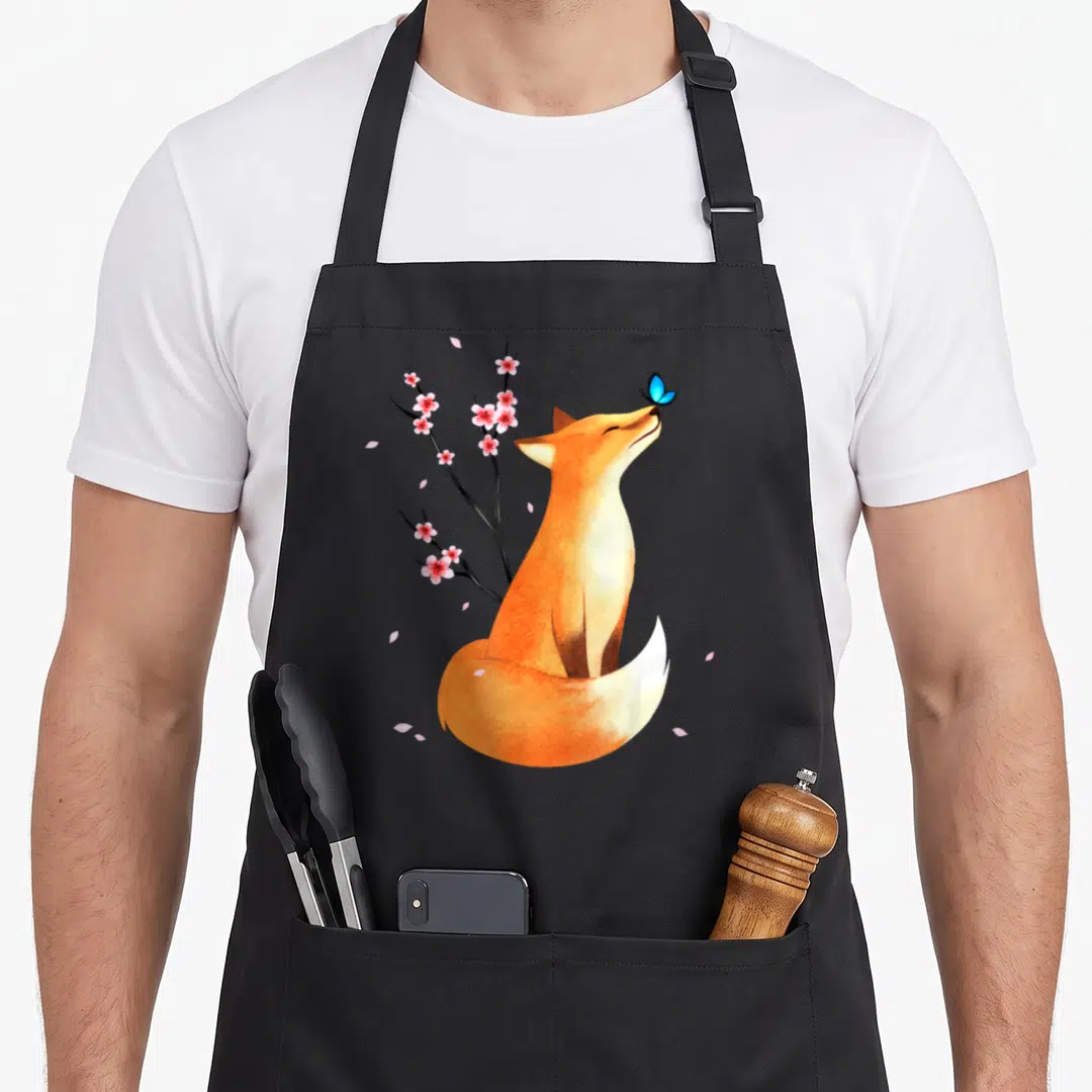 Cherry fox print apron - Orange fox sitting under pink cherry blossoms with blue butterfly on nose — shown on a black cotton canvas apron against a white background
