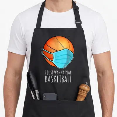 Play player basketball apron - Orange basketball wearing a light blue medical mask above white text reading I Just — shown on a black cotton canvas apron against a white background