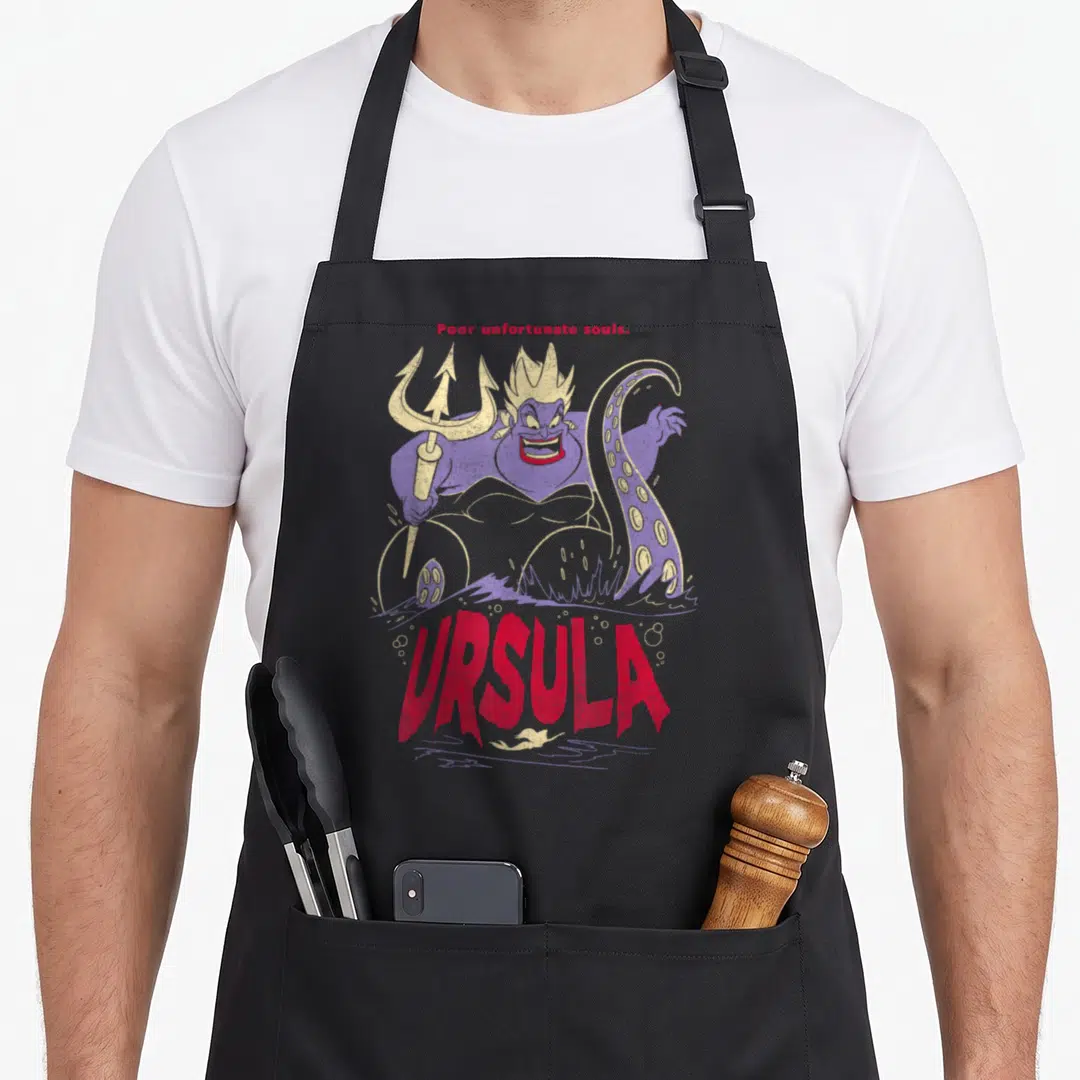Ursula villain novelty apron - Purple Ursula holding gold trident with red text Poor unfortunate souls and URSULA — shown on a black cotton canvas apron against a white background