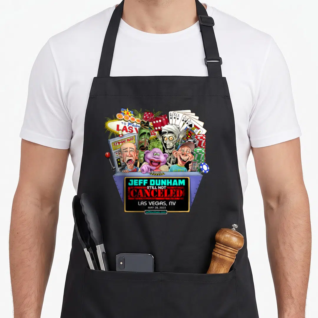Las hollywood apron - Ventriloquist puppets behind stage sign reading Jeff Dunham Still Not Canceled Las Vegas NV — shown on a black cotton canvas apron against a white background
