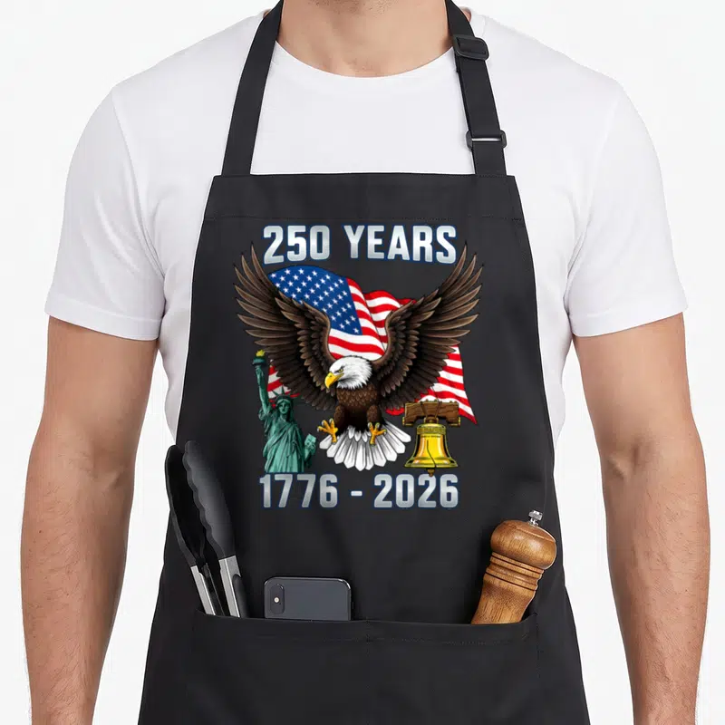 Anniversary patriotic 4th of july apron - Bald eagle over waving flag with Statue of Liberty and Liberty Bell flanking — shown on a black cotton canvas apron against a white background
