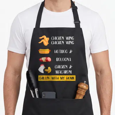 Viral hot dog apron - Cartoon chicken wings, hotdog, bologna, chicken head, macaroni with white text and yellow banner — shown on a black cotton canvas apron against a white background