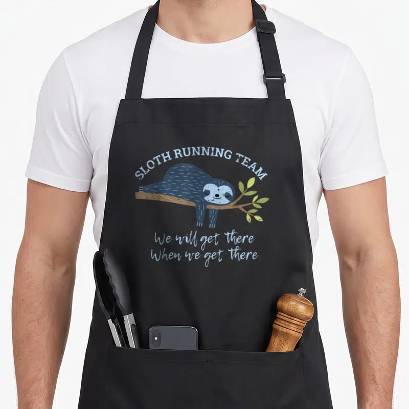 Jogging sloth apron - Blue cartoon sloth hanging from branch with SLOTH RUNNING TEAM text — shown on a black cotton canvas apron against a white background