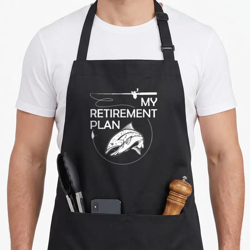 Retirement fishing aprons - White My Retirement Plan text with fishing rod and fish line art on black — shown on a black cotton canvas apron against a white background