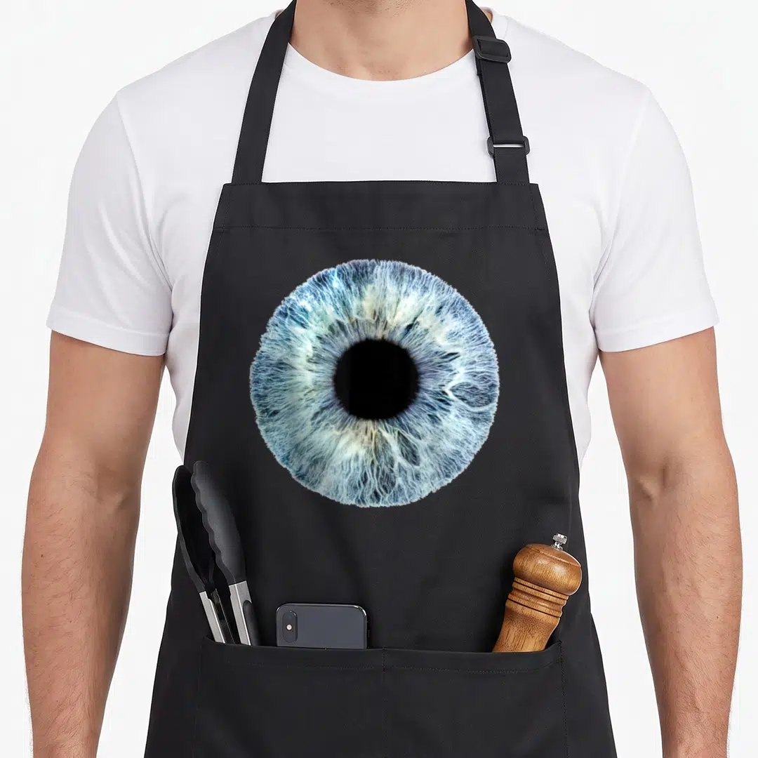 Eyeball optometrist apron - Close-up blue human eye iris with white and black details — shown on a black cotton canvas apron against a white background