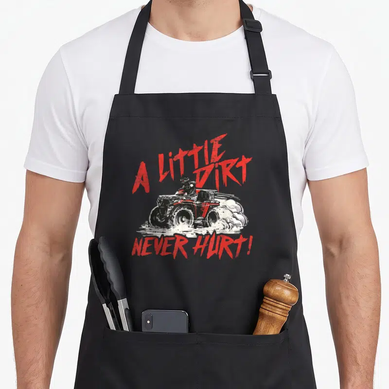 Dirt wheeler guy apron - Red and white distressed ATV rider with text A Little Dirt Never Hurt — shown on a black cotton canvas apron against a white background