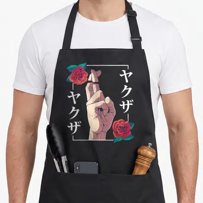 Broken goth apron - Hand with crossed fingers, red roses, and vertical Japanese text in white frame — shown on a black cotton canvas apron against a white background