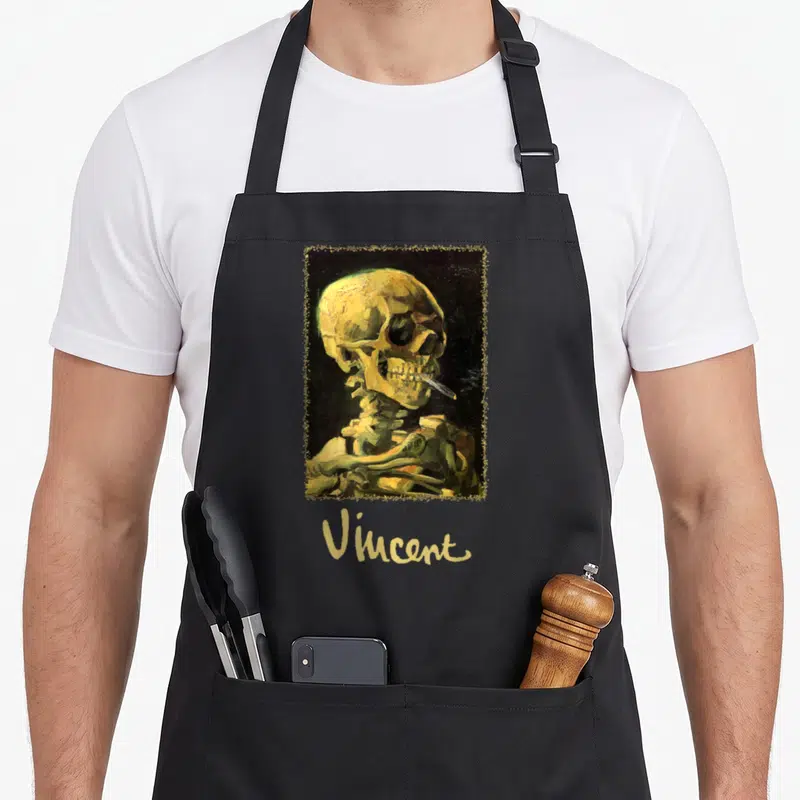 Skull van gogh apron - Yellow and black skeleton smoking cigarette inside distressed frame with Vincent text below — shown on a black cotton canvas apron against a white background