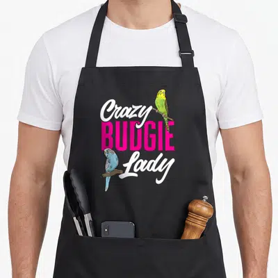 Parakeet budgie bird apron - Crazy BUDGIE Lady text with green and blue budgies on wooden perches — shown on a black cotton canvas apron against a white background