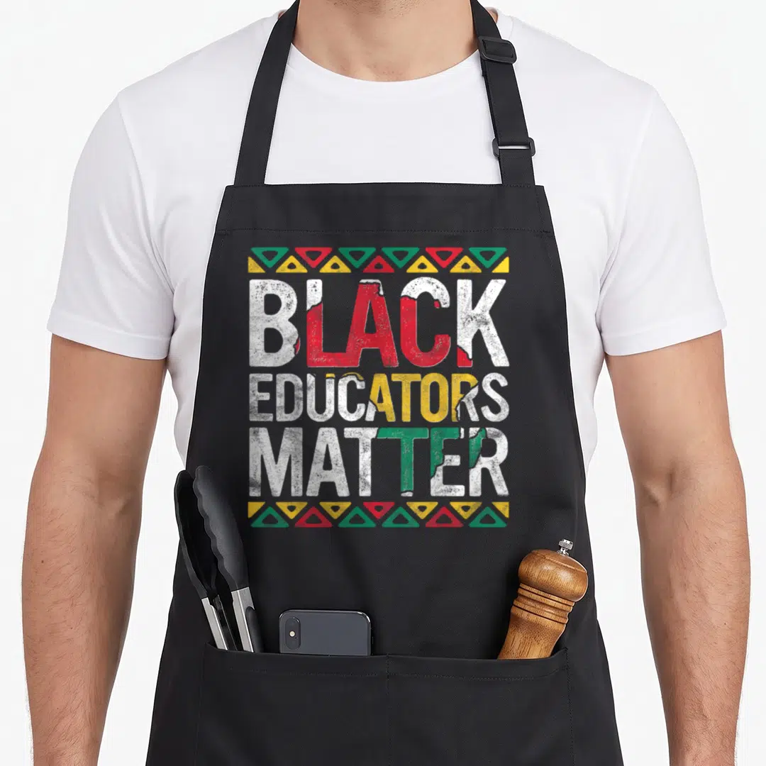 Pride teacher apron - Stacked BLACK EDUCATORS MATRE text with red yellow green fills and triangle borders — shown on a black cotton canvas apron against a white background