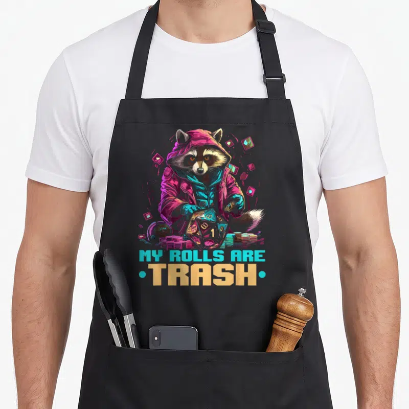 Role playing gaming apron - Raccoon in hoodie holding d20 die with MY ROLLS ARE TRASH text in neon colors — shown on a black cotton canvas apron against a white background