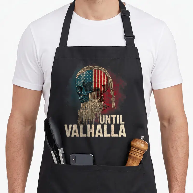Valhalla viking apron - Distressed skull with US flag pattern, bullet crown, magazine beard, and stacked text — shown on a black cotton canvas apron against a white background