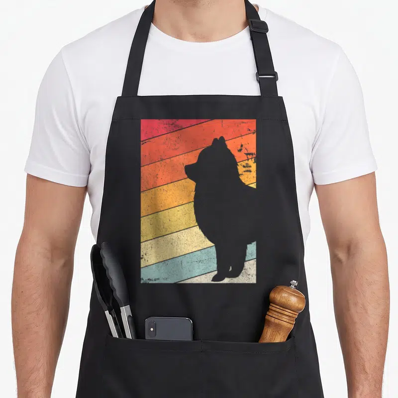 Pomeranian samoyed apron - Grey dog silhouette against diagonal red orange yellow and blue retro stripes — shown on a black cotton canvas apron against a white background