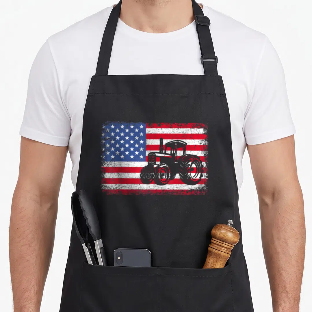 Flag farm apron - Grey tractor silhouette over distressed red white blue American flag pattern — shown on a black cotton canvas apron against a white background
