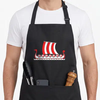 Scandinavia viking apron - Red and white viking ship with striped sail and seven cross shields on waves — shown on a black cotton canvas apron against a white background