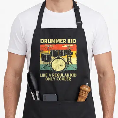 Drumline drum apron - Retro drum kit on red yellow green stripes with text DRUMMER KID LIKE A REGULAR KID ONLY COOLER — shown on a black cotton canvas apron against a white background