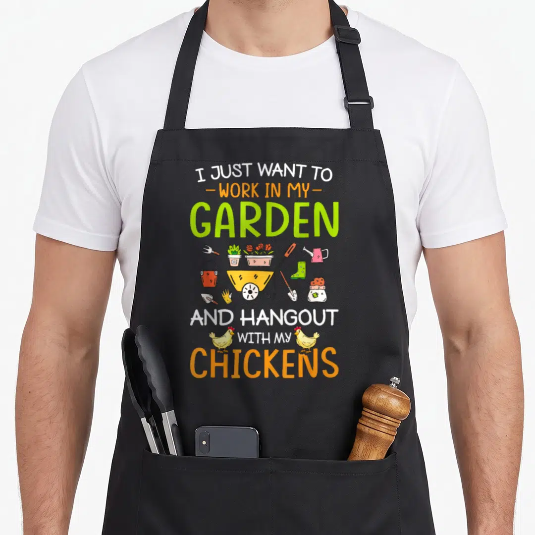 Hangout chicken apron - Cartoon gardening tools and two yellow chickens surround stacked text about working in a garden — shown on a black cotton canvas apron against a white background