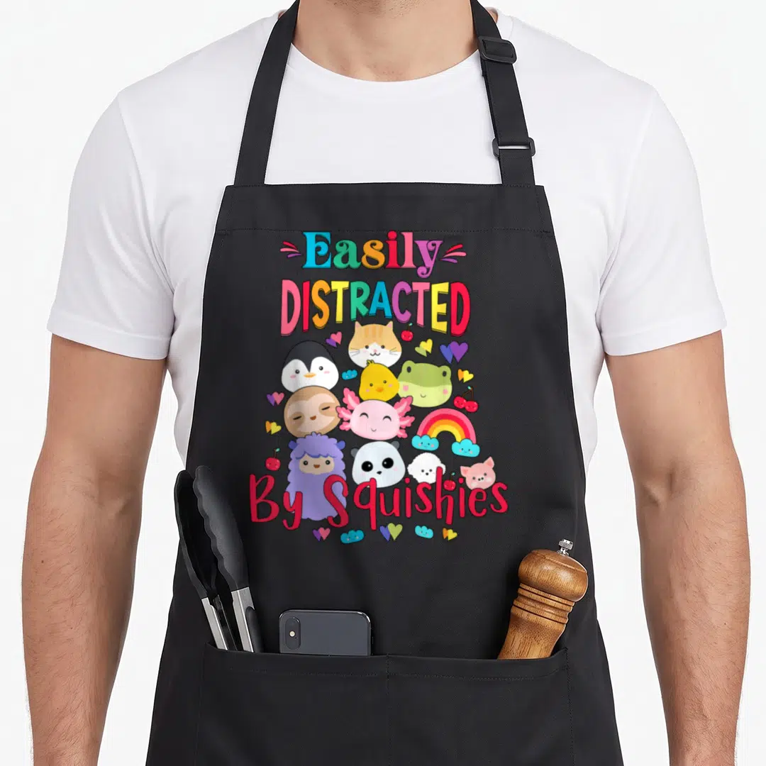 Squishy animal apron - Cartoon animals rainbow hearts cherry text easily distracted by squishies — shown on a black cotton canvas apron against a white background