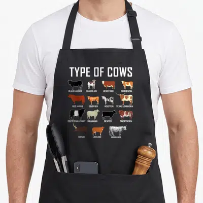 Farmer costume cow apron - 15 cattle breed silhouettes with names like Black Angus and Texas Longhorn in a grid layout — shown on a black cotton canvas apron against a white background