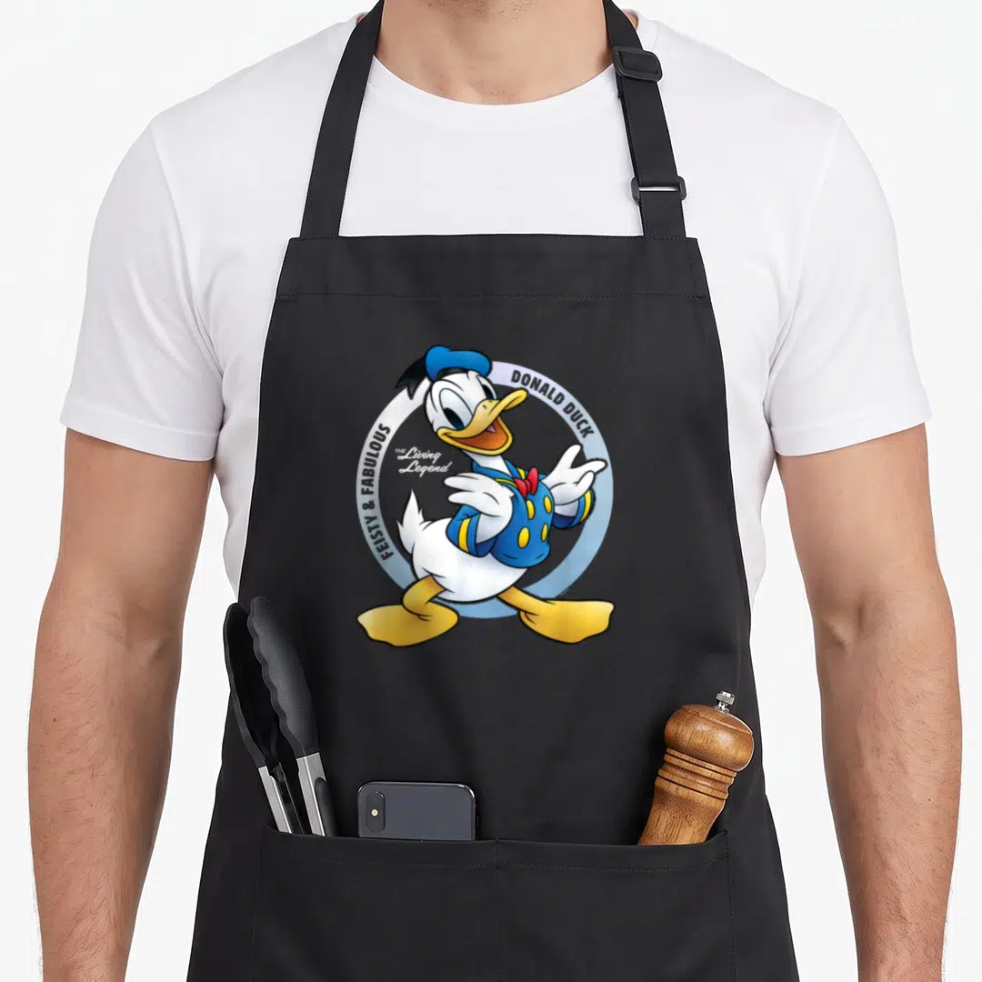 90th anniversary apron - Donald Duck cartoon figure inside blue circle with Feisty and Fabulous text — shown on a black cotton canvas apron against a white background