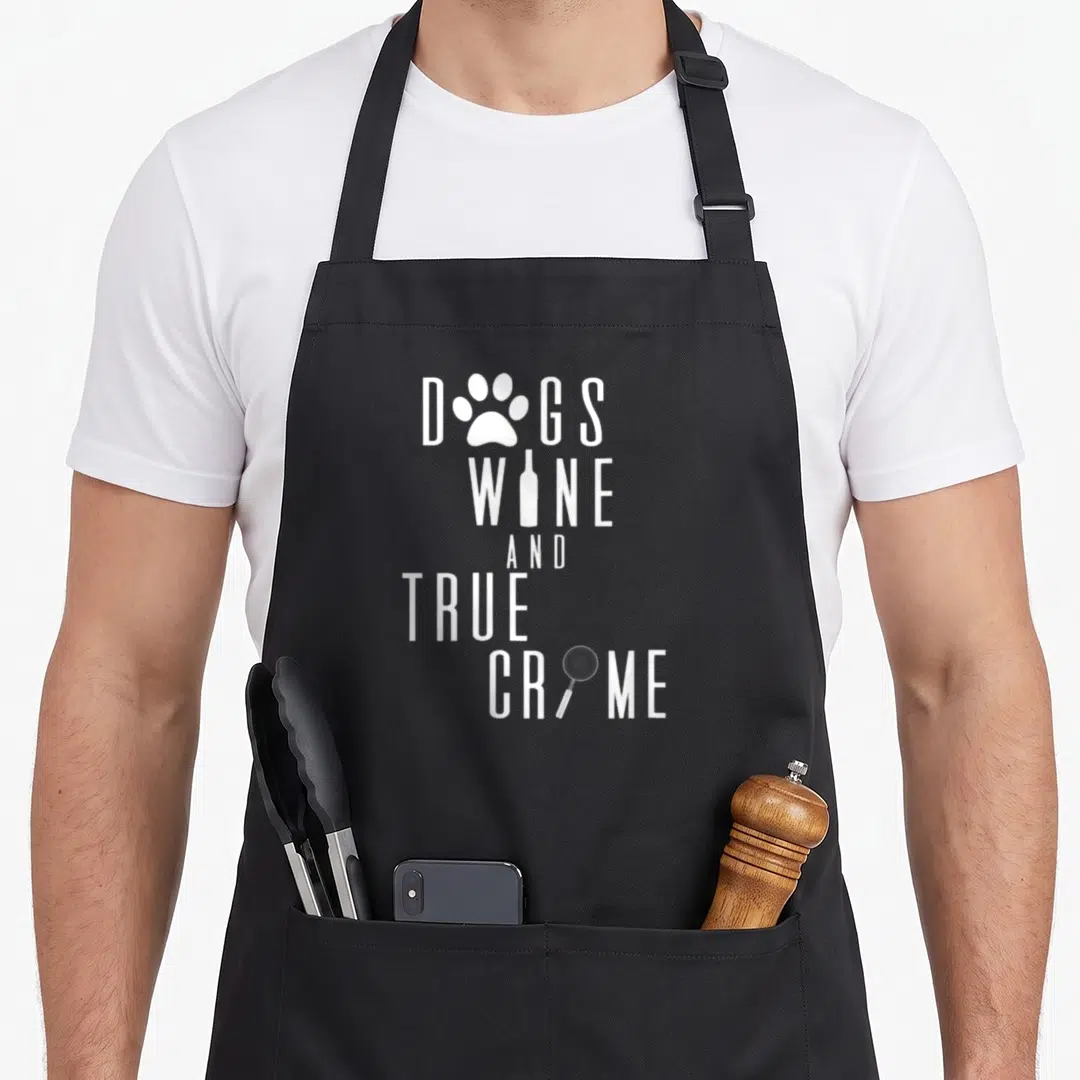 Wine crime dog apron - Stacked white text DOGS WINE AND TRUE CRIME with paw, bottle, and magnifying glass icons on grey — shown on a black cotton canvas apron against a white background