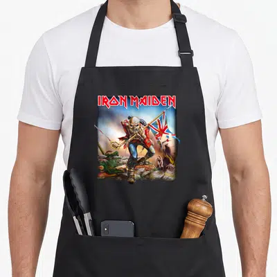 Trooper camping apron - IRON MAIDEN text above skeleton soldier holding rifle and flag among rocks — shown on a black cotton canvas apron against a white background