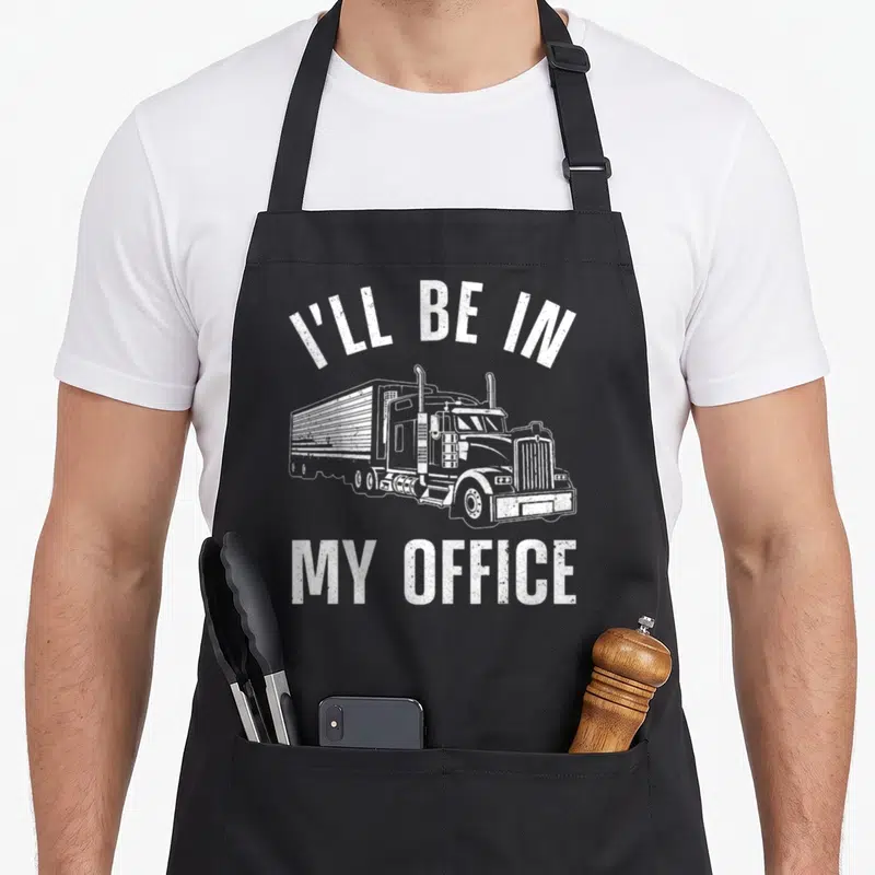 Trucker rig truck apron - White semi-truck drawing with I'll Be In My Office text in distressed font — shown on a black cotton canvas apron against a white background
