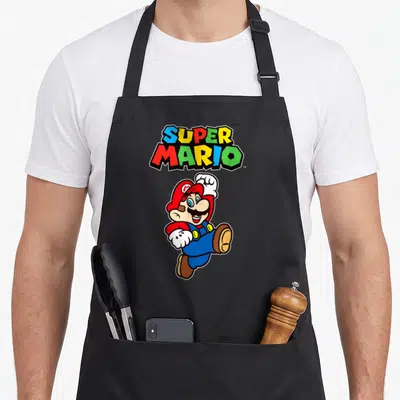 Jump character aprons - Super Mario logo above jumping Mario in red blue yellow and green cartoon style — shown on a black cotton canvas apron against a white background