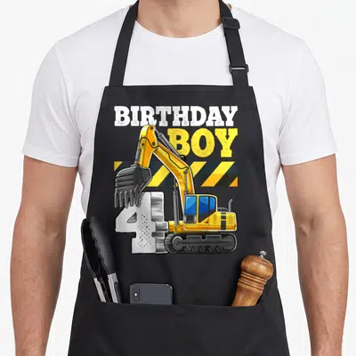 4th vehicle apron - Yellow excavator bucket on white number 4 under BIRTHDAY BOY text with hazard stripes — shown on a black cotton canvas apron against a white background