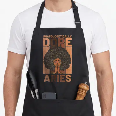 History horoscope apron - Unapologetically Dope Aries woman silhouette in copper brown grey and yellow — shown on a black cotton canvas apron against a white background