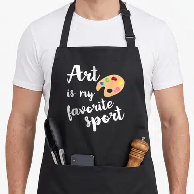 Sport painter apron - White script text next to tan palette with red blue yellow green and pink blobs — shown on a black cotton canvas apron against a white background