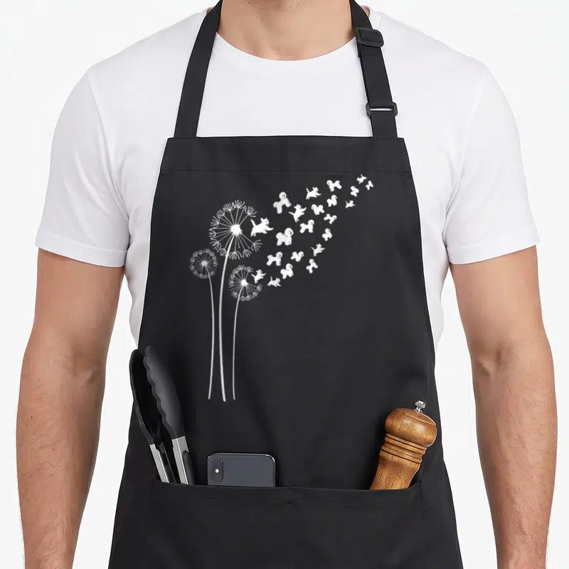 Dandelion dog apron - Three white dandelions with small fluffy dogs drifting as seeds towards the right — shown on a black cotton canvas apron against a white background