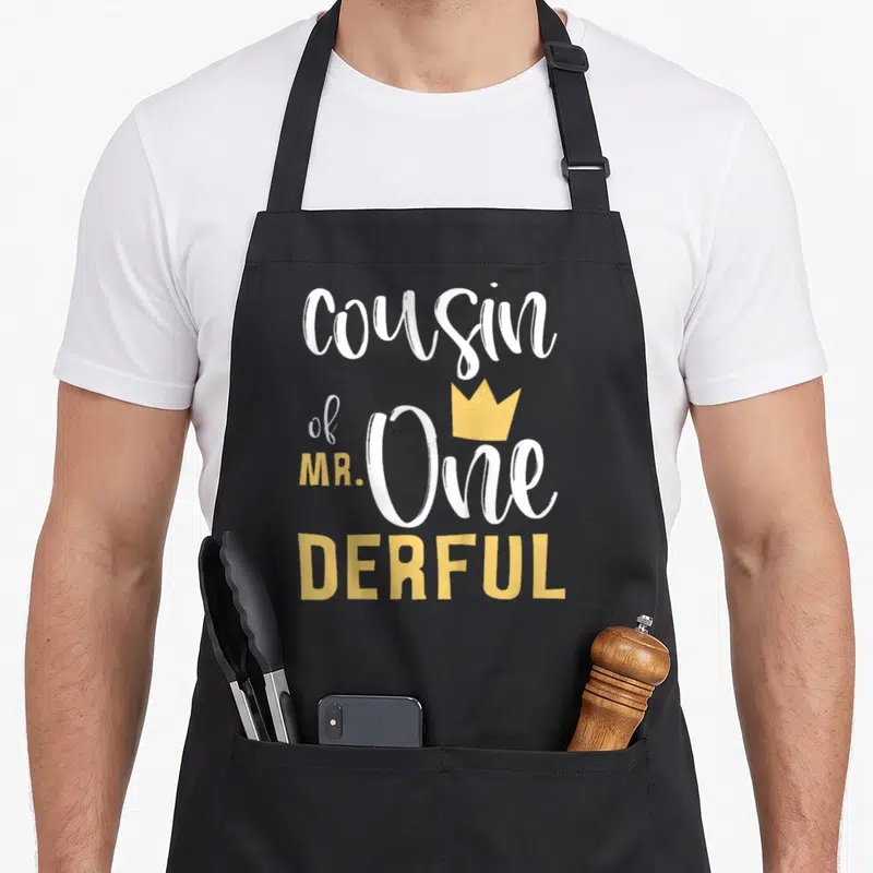 Cousin onederful birthday apron - White and yellow typography reading cousin of MR One DERFUL with a yellow crown — shown on a black cotton canvas apron against a white background