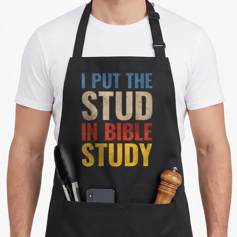 Cute stud bible study apron - Stacked I PUT THE STUD IN BIBLE STUDY text in blue beige red yellow distressed font — shown on a black cotton canvas apron against a white background