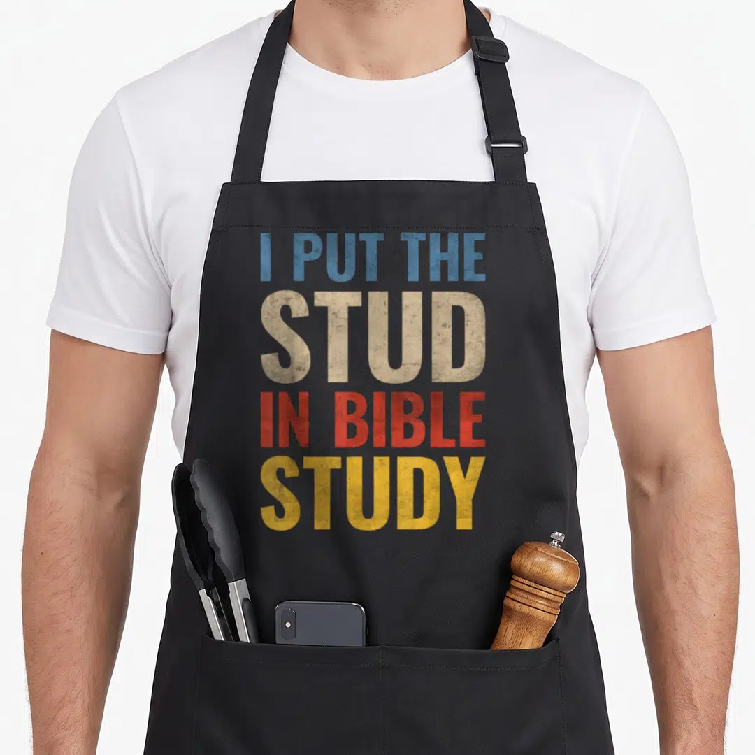 Cute stud bible study apron - Stacked I PUT THE STUD IN BIBLE STUDY text in blue beige red yellow distressed font — shown on a black cotton canvas apron against a white background