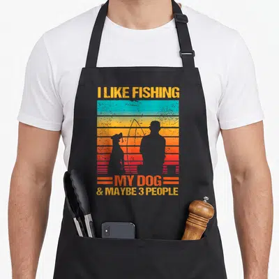 Fishing dog apron - Retro sunset graphic with fisherman and dog silhouettes and text I LIKE FISHING MY DOG & MAYBE 3 — shown on a black cotton canvas apron against a white background