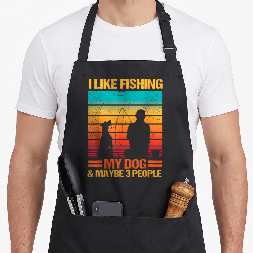Fishing dog apron - Retro sunset graphic with fisherman and dog silhouettes and text I LIKE FISHING MY DOG & MAYBE 3 — shown on a black cotton canvas apron against a white background