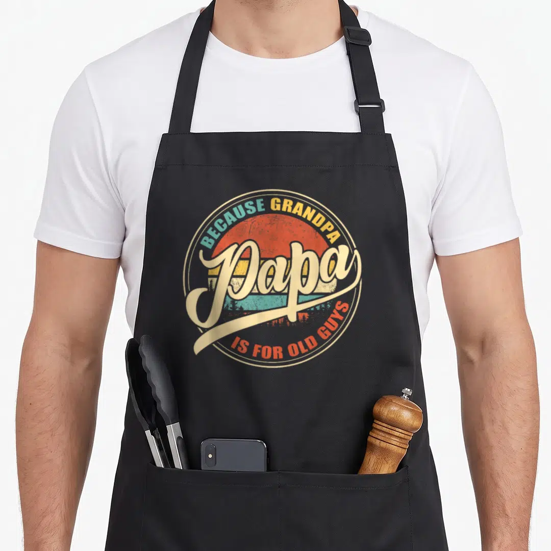 Papa sunset grandpa apron - Retro striped sun with forest silhouette and Because Grandpa Papa Is For Old Guys text — shown on a black cotton canvas apron against a white background