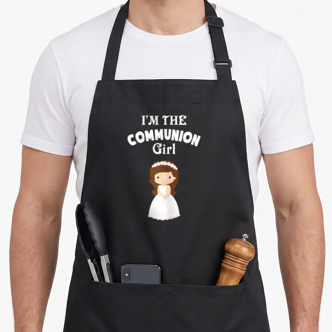 Costume communion aprons - I'M THE COMMUNION Girl text above cartoon girl in white dress with flower crown holding — shown on a black cotton canvas apron against a white background
