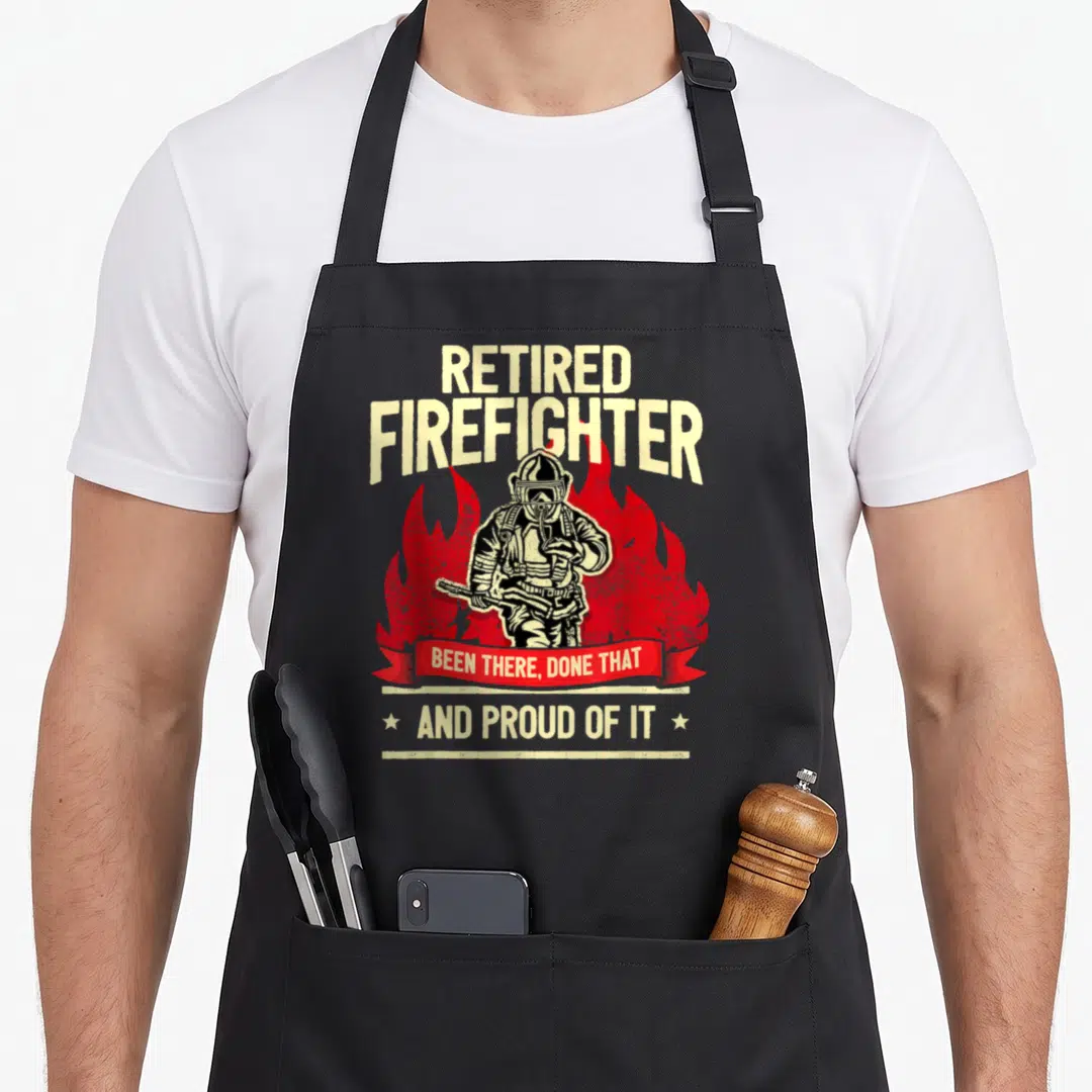 Fire retirement apron - Distressed RETIRED FIREFIGHTER text with red flames and helmeted figure holding hose — shown on a black cotton canvas apron against a white background