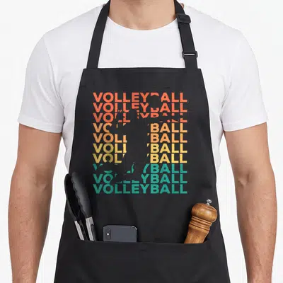 Retro player volleyball apron - Grey volleyball player silhouette over ten stacked VOLLEYBALL words in orange yellow — shown on a black cotton canvas apron against a white background
