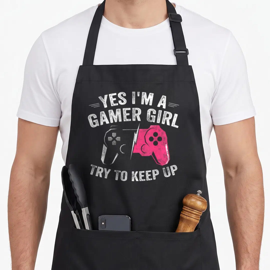 Gamer video gaming apron - Distressed white and pink split game controller with arched text yes i'm a gamer girl try — shown on a black cotton canvas apron against a white background