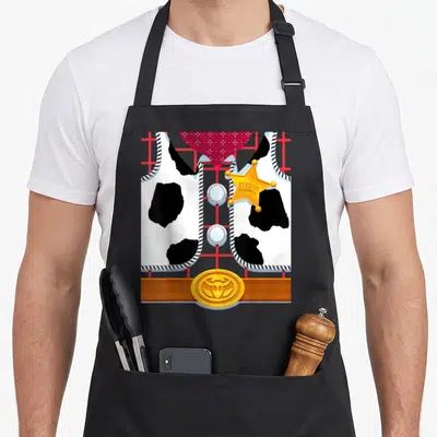 Sheriff halloween apron - Cartoon cow-print vest with gold sheriff star, red bandana, and brown belt buckle — shown on a black cotton canvas apron against a white background