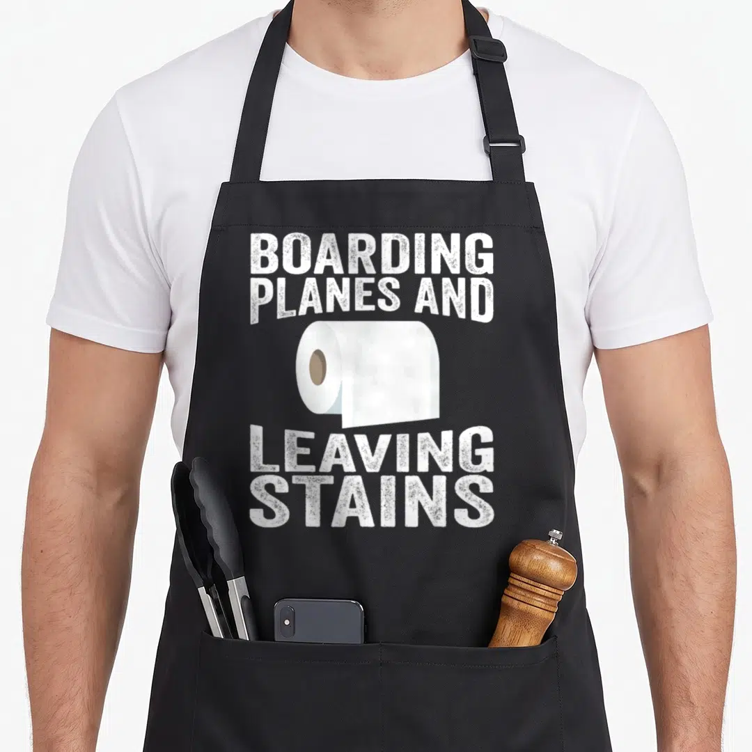 Boarding joke apron - White toilet paper roll centered between distressed text reading BOARDING PLANES AND LEAVING — shown on a black cotton canvas apron against a white background
