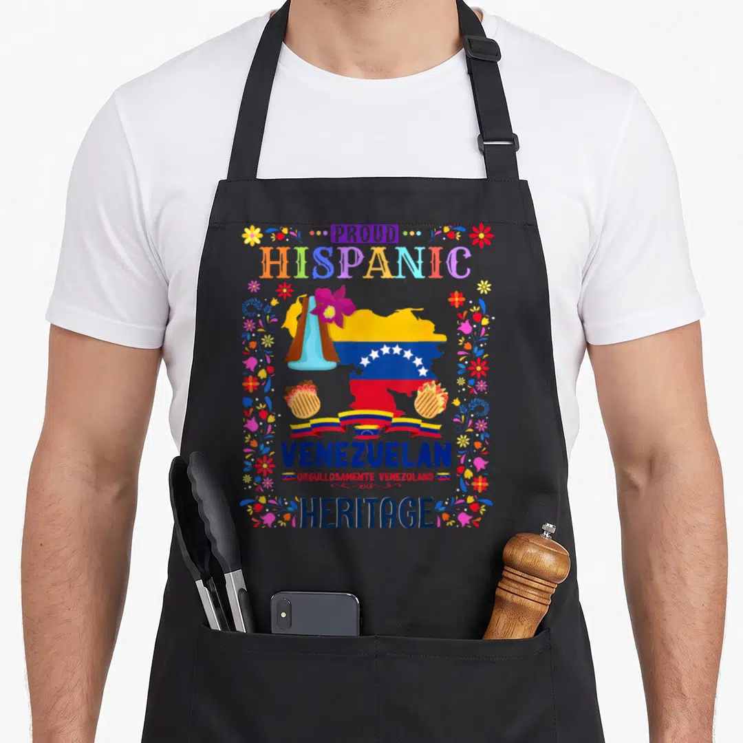 Latin chef outfit with apron - Venezuelan map with floral borders, arepas, ribbon, and text PROUD HISPANIC VENEZUELAN — shown on a black cotton canvas apron against a white background