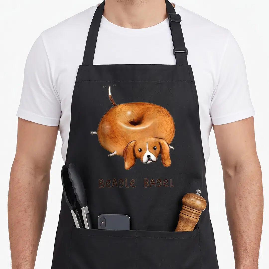 Bagel beagle apron - Cartoon brown and white beagle shaped like a bagel with text below — shown on a black cotton canvas apron against a white background