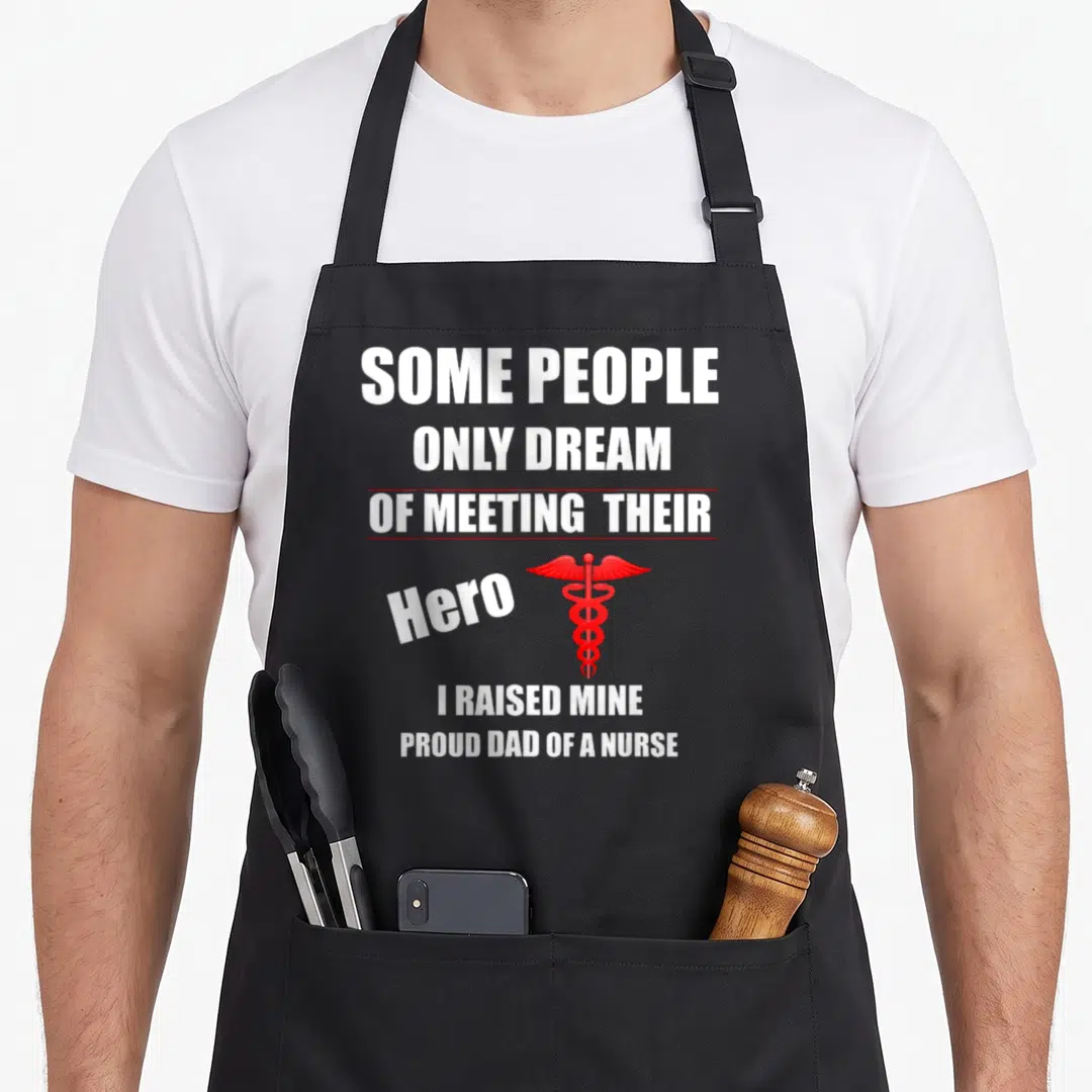 Raised nurses apron - Stacked white text reading I Raised Mine with a red caduceus symbol beside the word Hero — shown on a black cotton canvas apron against a white background