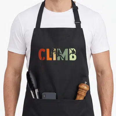Bouldering mountain climbing apron - CLIMB text in red orange yellow and green with silhouette figures climbing — shown on a black cotton canvas apron against a white background