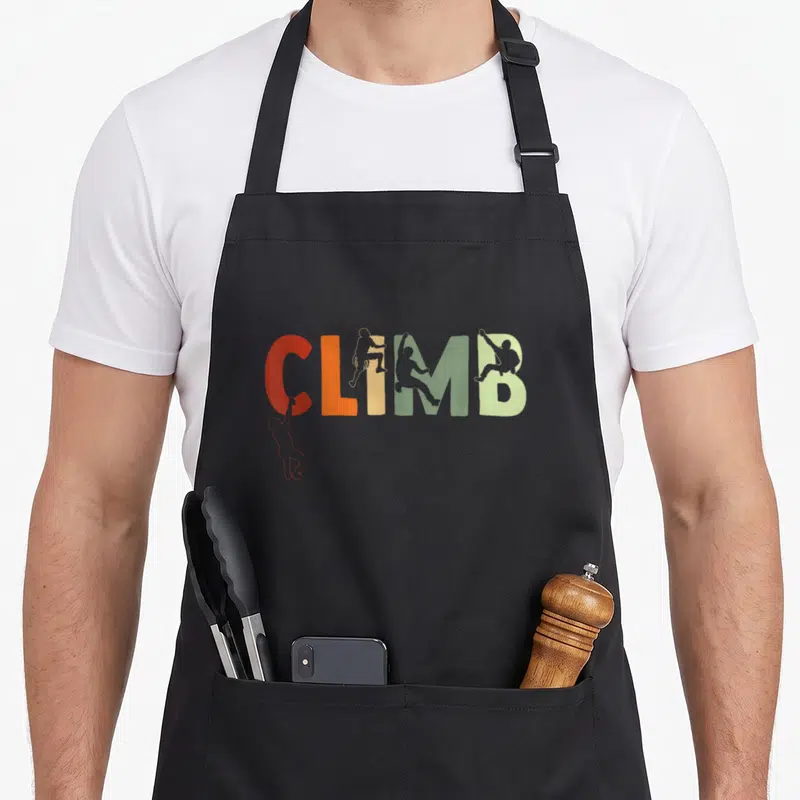 Bouldering mountain climbing apron - CLIMB text in red orange yellow and green with silhouette figures climbing — shown on a black cotton canvas apron against a white background